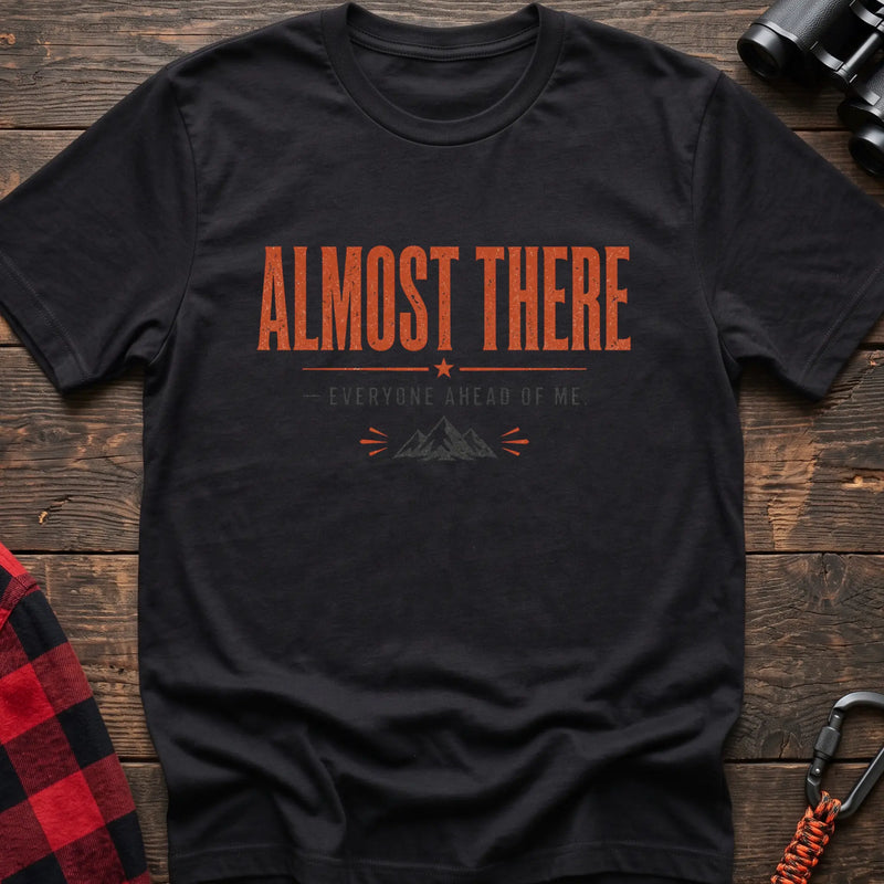 Black cotton t-shirt with a mountain graphic and Almost There Everyone Ahead of Me text on rustic wood