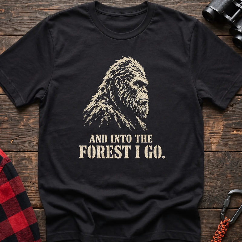 Black cotton t-shirt with a Bigfoot graphic and And Into the Forest I Go text on rustic wood