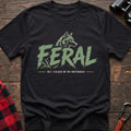 Black cotton t-shirt with a wolf graphic and Feral But I Yielded on the Switchback text on rustic wood