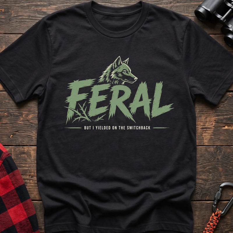 Black cotton t-shirt with a wolf graphic and Feral But I Yielded on the Switchback text on rustic wood