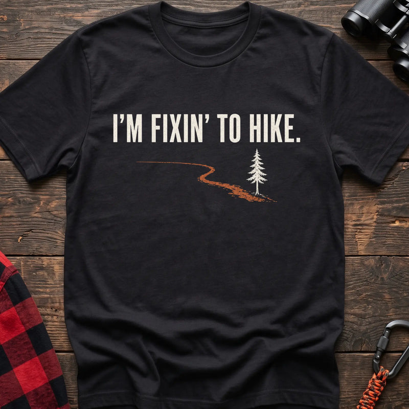 Black cotton t-shirt with a trail and pine graphic and I’m Fixin’ to Hike text on rustic wood
