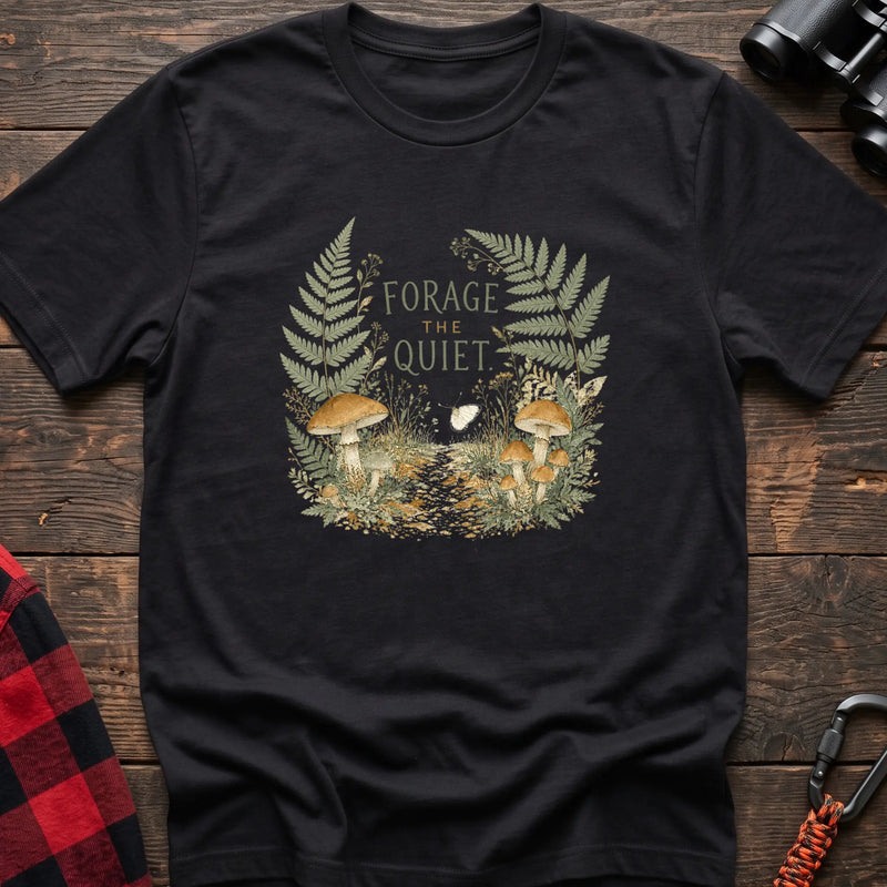 Black cotton t-shirt with a mushroom and fern graphic and Forage the Quiet text on rustic wood