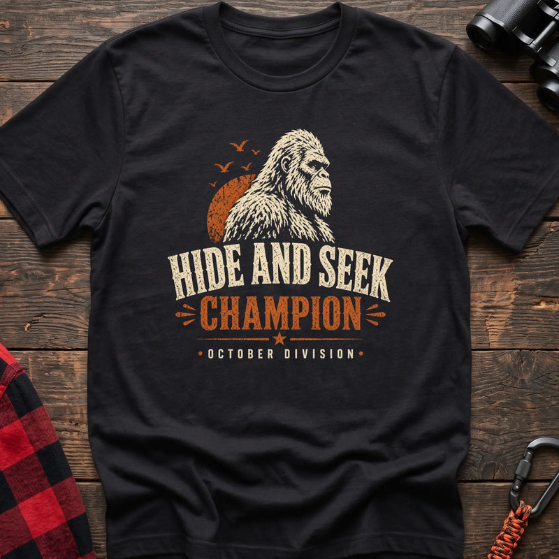 Black cotton t-shirt with a Bigfoot graphic and Hide and Seek Champion October Division text on rustic wood