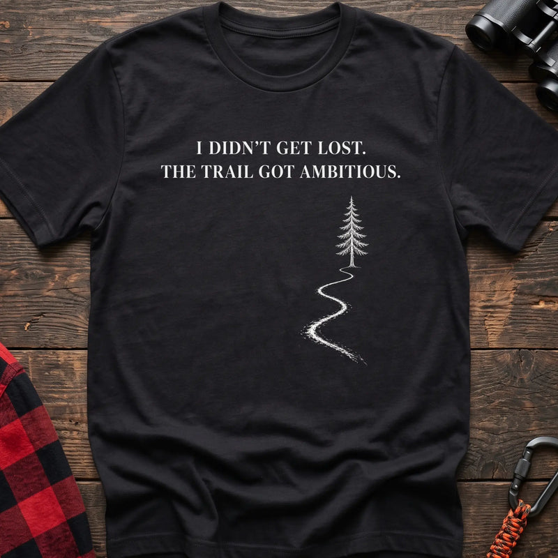 Black cotton t-shirt with a winding trail graphic and I Didn’t Get Lost The Trail Got Ambitious text on rustic wood