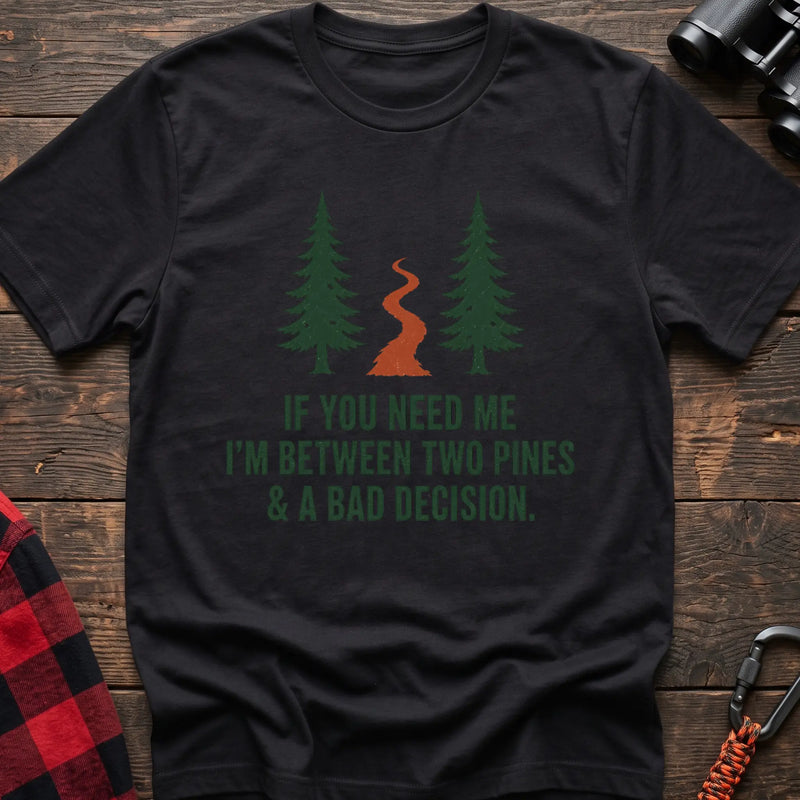 Black cotton t-shirt with two pines and a trail graphic and If You Need Me I’m Between Two Pines and a Bad Decision text on rustic wood