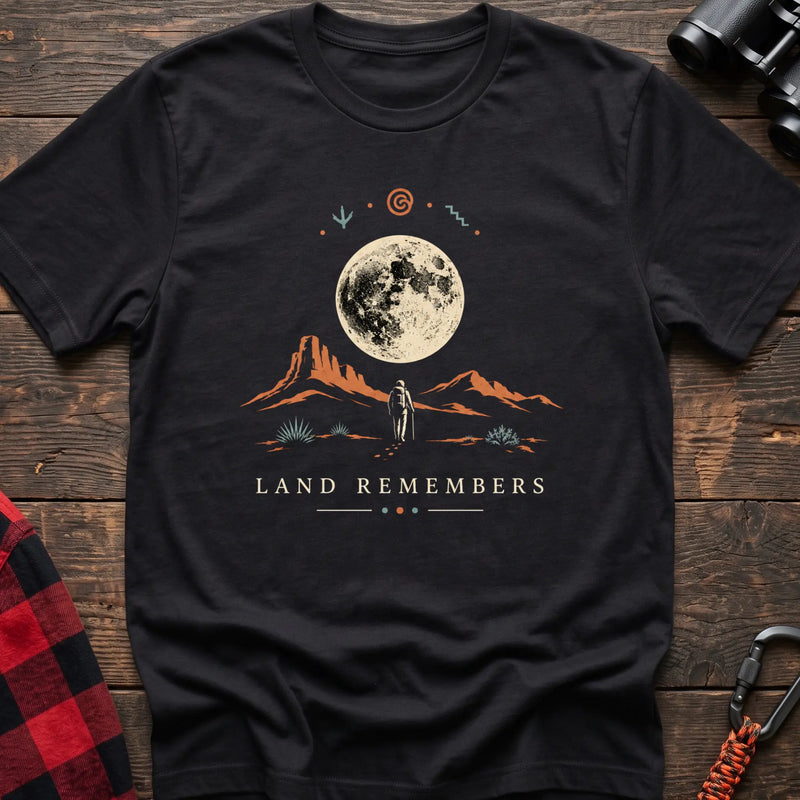 Black cotton t-shirt with a desert hiker and full moon graphic and Land Remembers text on rustic wood