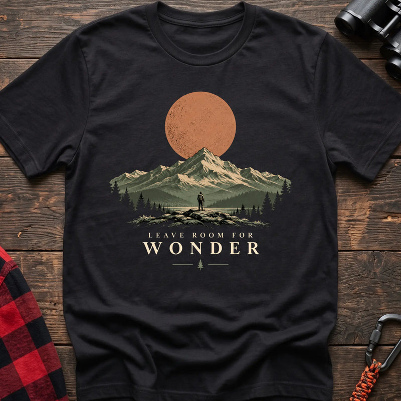 Black cotton t-shirt with a hiker and mountain sunset graphic and Leave Room for Wonder text on rustic wood