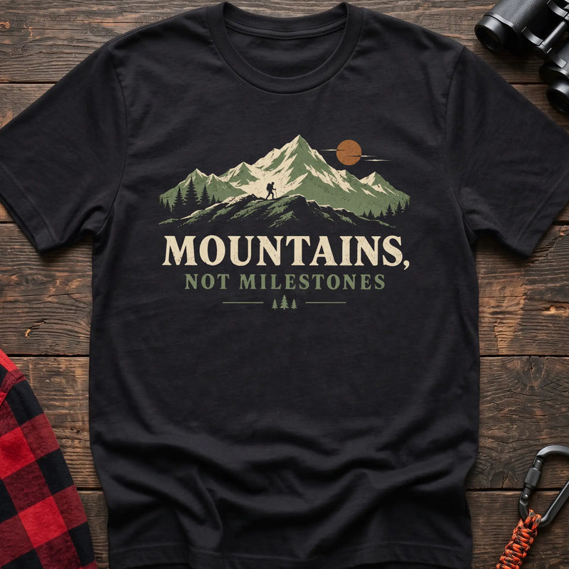 Black cotton t-shirt with a hiker and mountain graphic and Mountains Not Milestones text on rustic wood