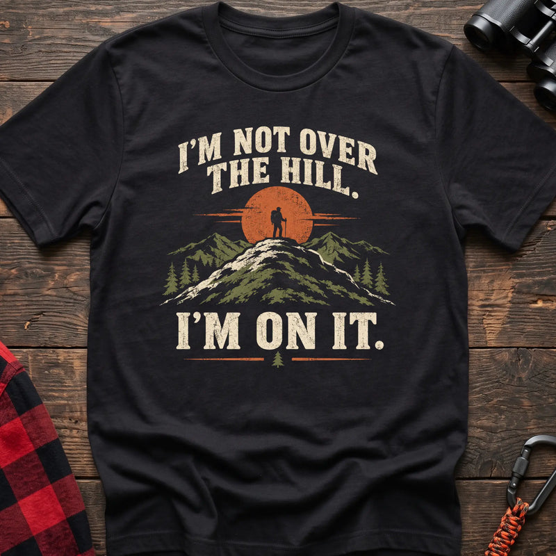 Black cotton t-shirt with a hiker on a summit graphic and I’m Not Over the Hill I’m On It text on rustic wood