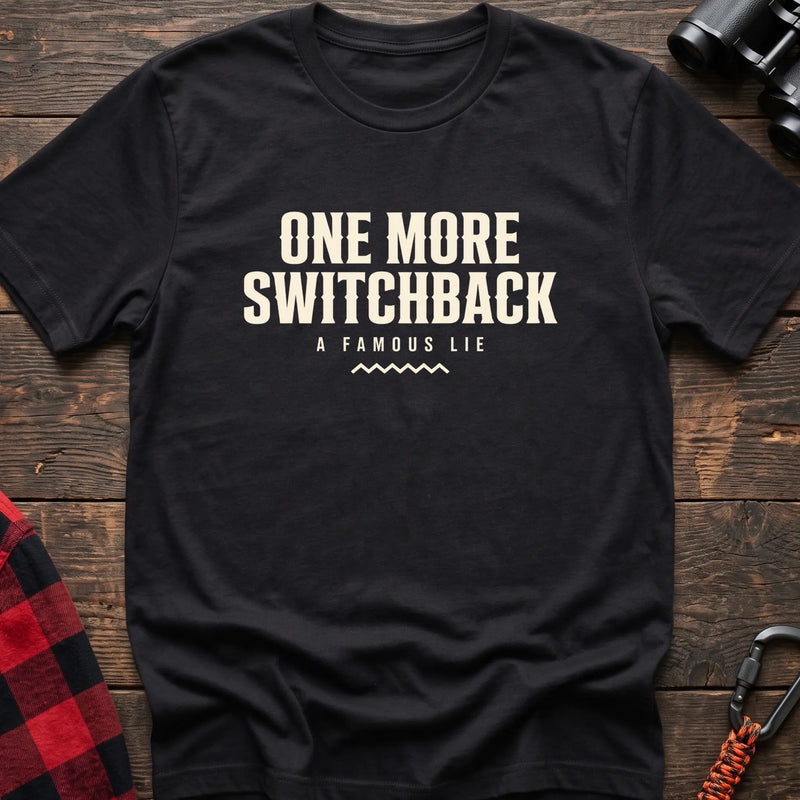 Black cotton t-shirt with One More Switchback A Famous Lie text on rustic wood