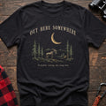 Black cotton t-shirt with a moonlit moose and pines graphic and Out Here Somewhere text on rustic wood