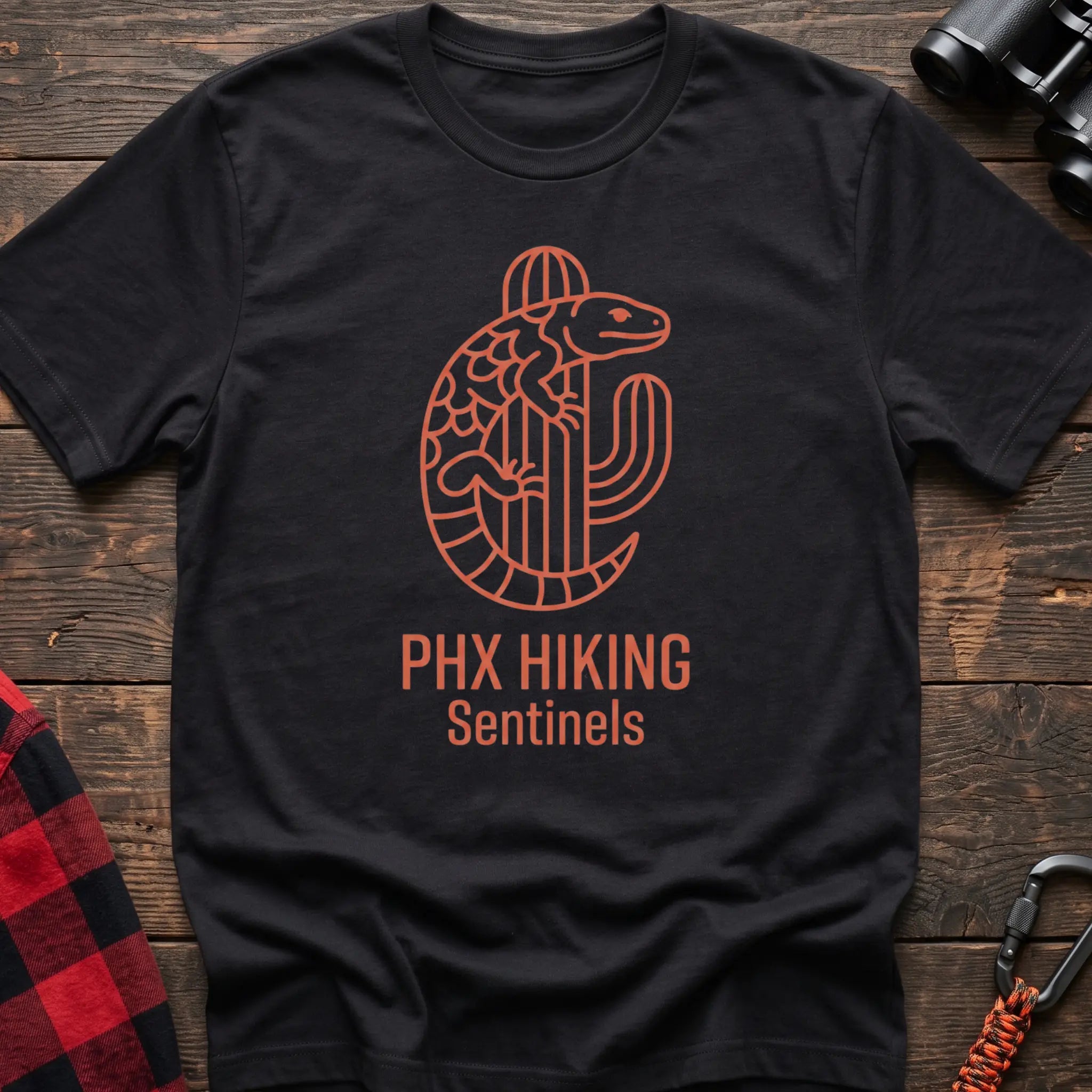 Black t-shirt with orange line-art Gila monster wrapped around a saguaro cactus and the text “PHX HIKING Sentinels”