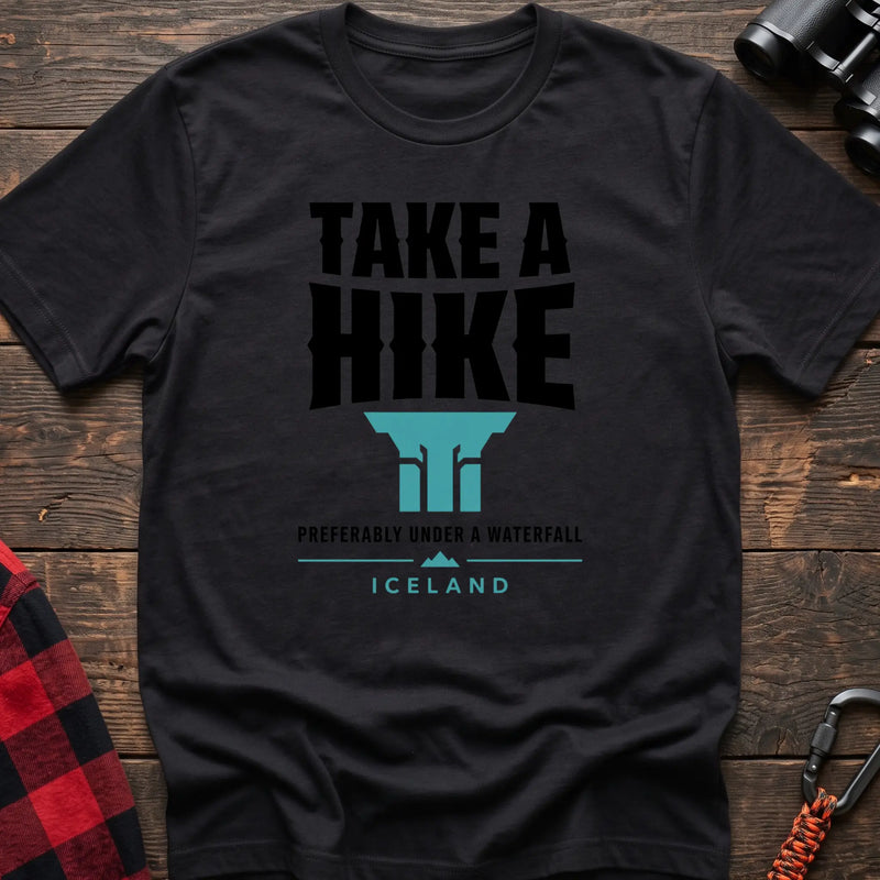 Black cotton t-shirt with a waterfall graphic and Take a Hike Preferably Under a Waterfall Iceland text on rustic wood