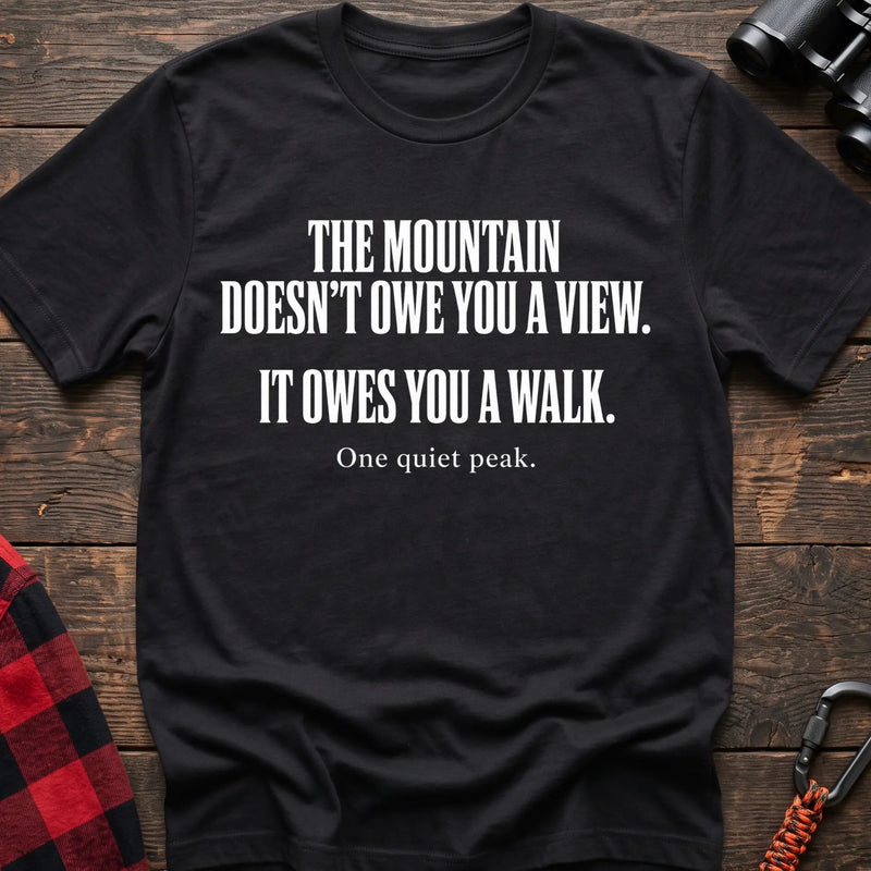 Black cotton t-shirt with The Mountain Doesn’t Owe You a View It Owes You a Walk text on rustic wood