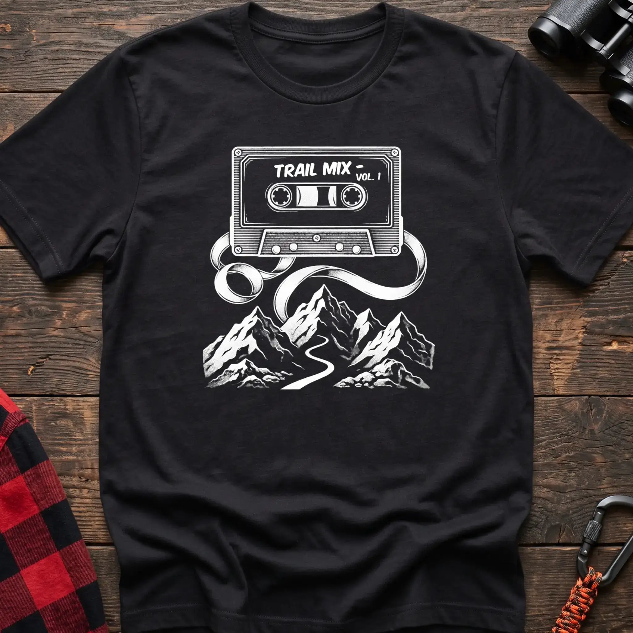 Black t-shirt with white cassette tape graphic labeled Trail Mix Vol. 1, with tape unspooling into a trail through mountains