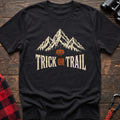Black cotton t-shirt with mountains, a jack-o’-lantern, and Trick or Trail text on rustic wood
