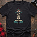 Black cotton t-shirt with a bootprint trail and mountain graphic and Walk Far Tread Light text on rustic wood