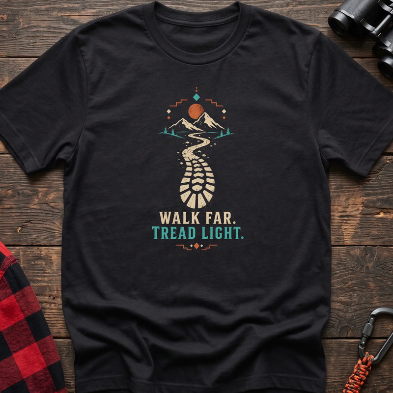 Black cotton t-shirt with a bootprint trail and mountain graphic and Walk Far Tread Light text on rustic wood