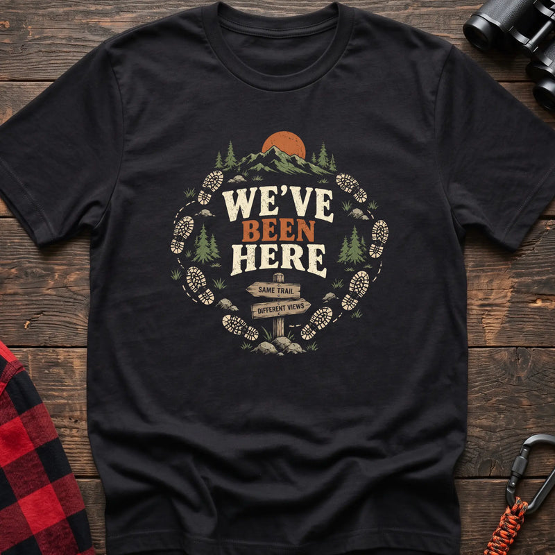 Black cotton t-shirt with a bootprint circle and trail sign graphic and We’ve Been Here text on rustic wood