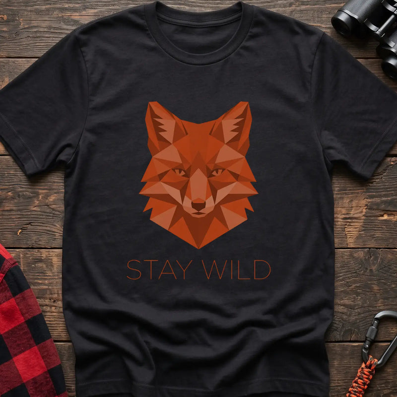 Black t-shirt with a geometric low-poly orange fox head and the text “STAY WILD” printed below in matching orange, laid flat on a wooden surface.