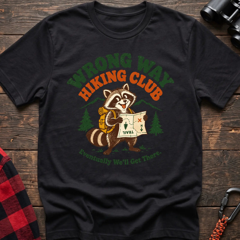 Black cotton t-shirt with a raccoon holding a map graphic and Wrong Way Hiking Club text on rustic wood
