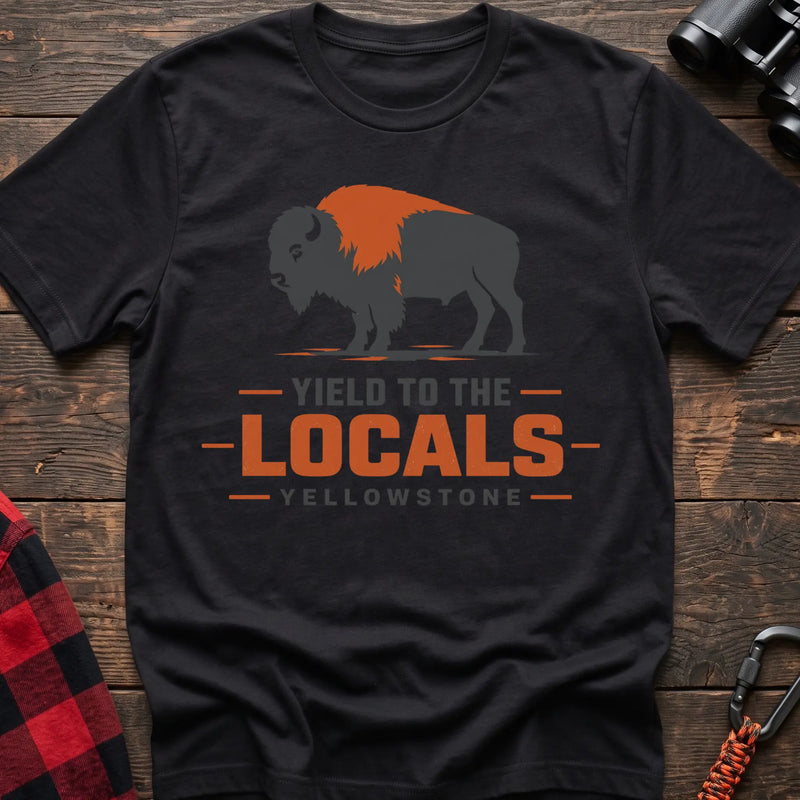 Black cotton t-shirt with a bison graphic and Yield to the Locals Yellowstone text on rustic wood