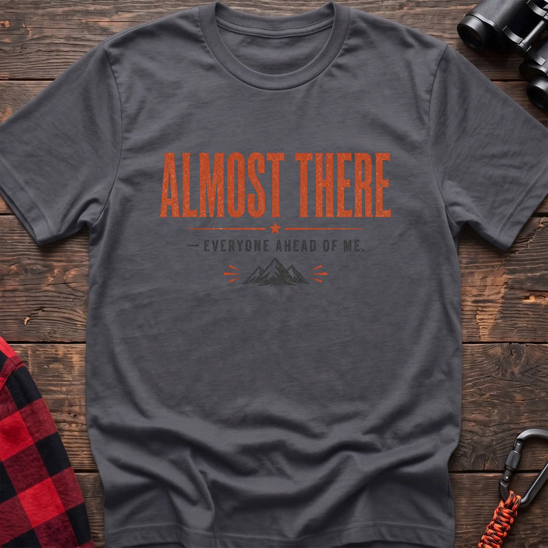 Charcoal cotton t-shirt with a mountain graphic and Almost There Everyone Ahead of Me text on rustic wood