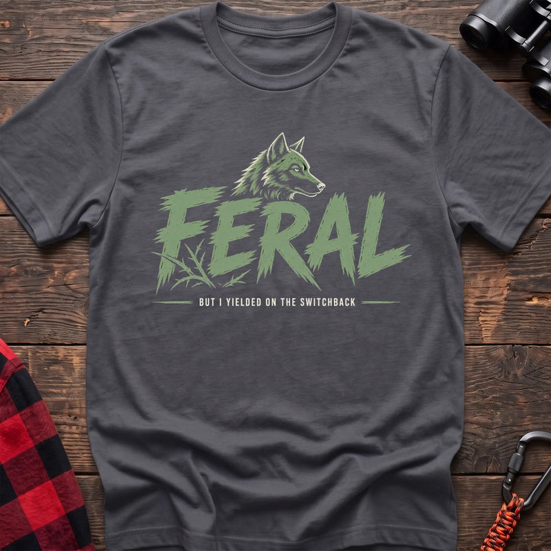 Charcoal cotton t-shirt with a wolf graphic and Feral But I Yielded on the Switchback text on rustic wood