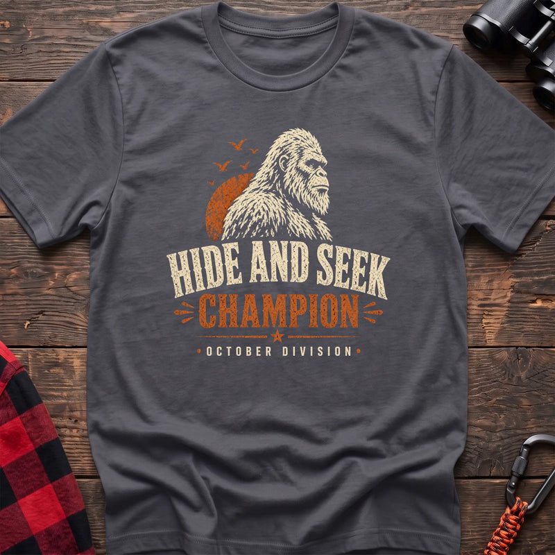 Charcoal cotton t-shirt with a Bigfoot graphic and Hide and Seek Champion October Division text on rustic wood