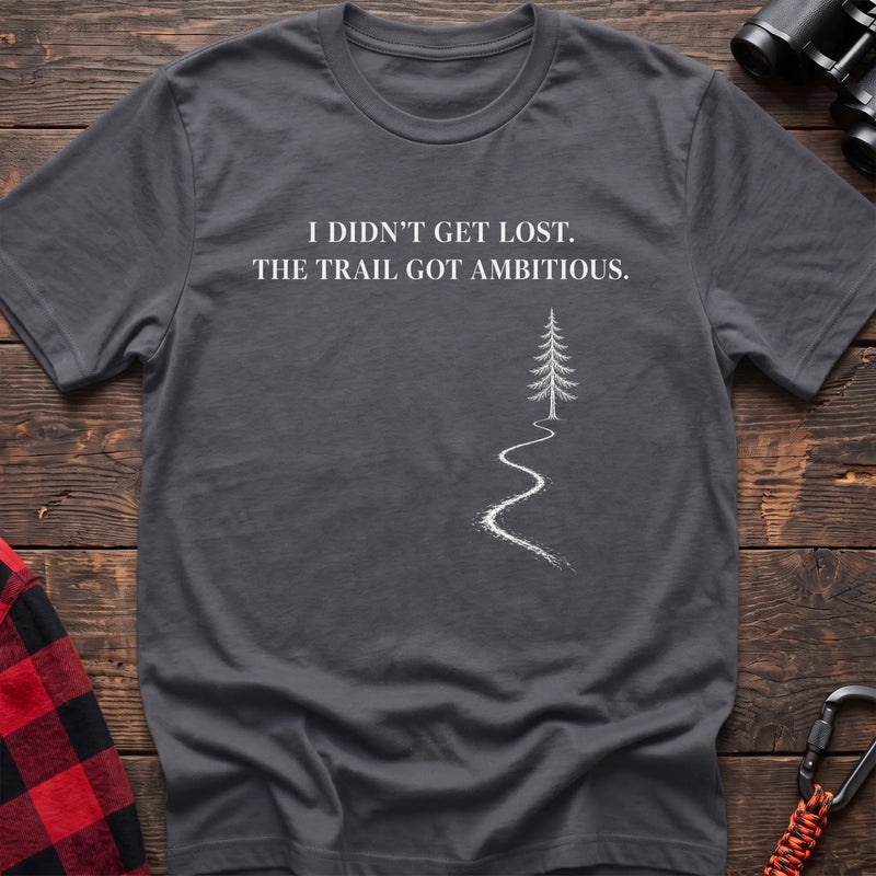 Charcoal cotton t-shirt with a winding trail graphic and I Didn’t Get Lost The Trail Got Ambitious text on rustic wood