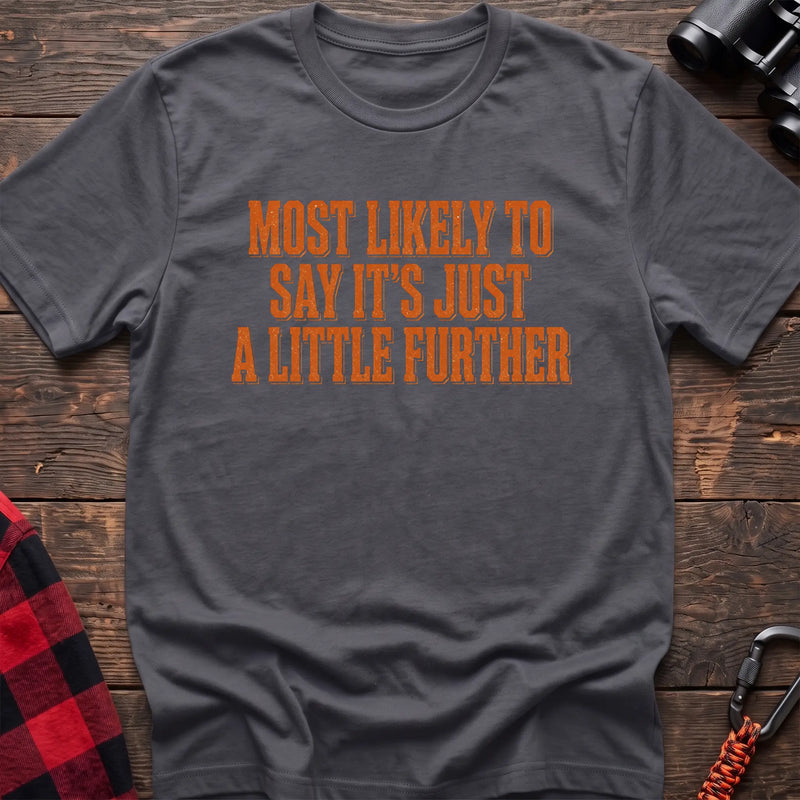 Charcoal cotton t-shirt with Most Likely to Say It’s Just a Little Further text on rustic wood