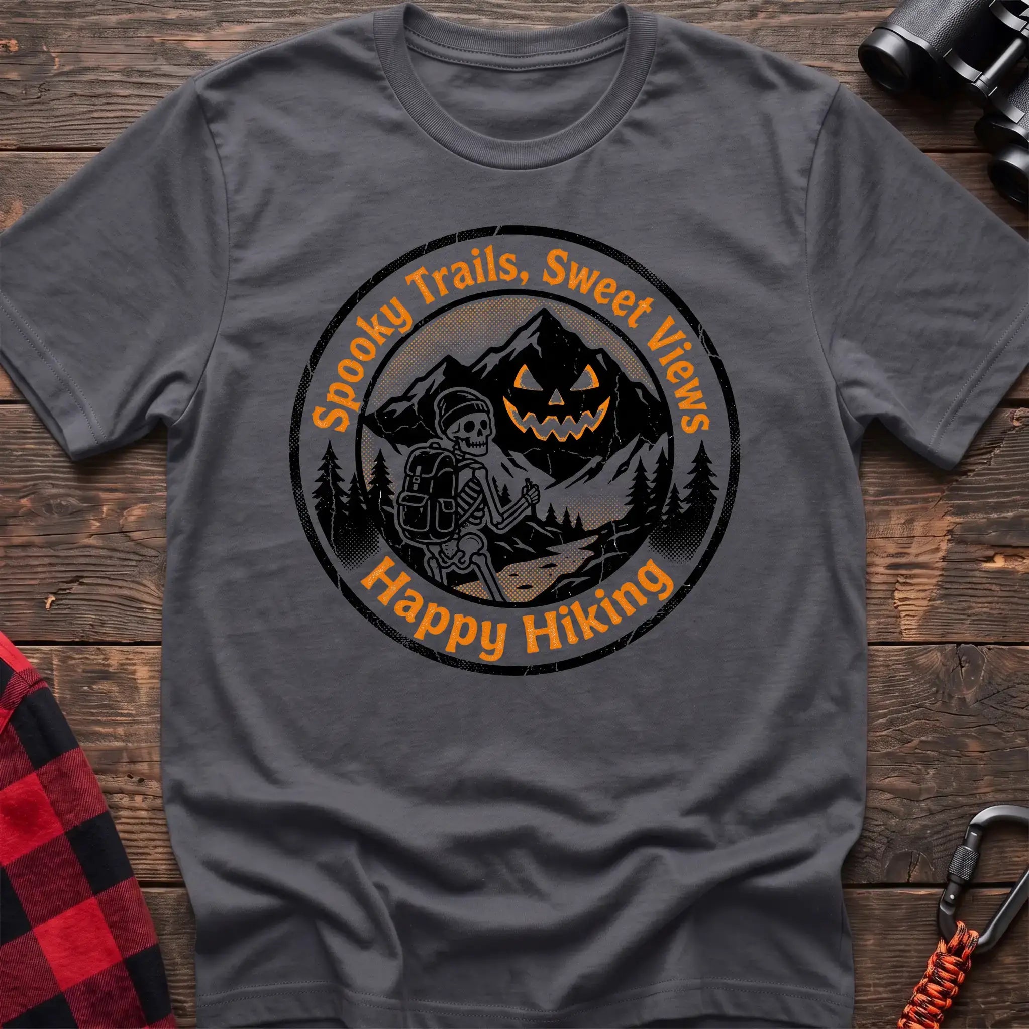 Charcoal t-shirt with circular graphic of a skeleton hiker giving a thumbs up in front of a jack-o-lantern mountain, reading Spooky Trails Sweet Views Happy Hiking