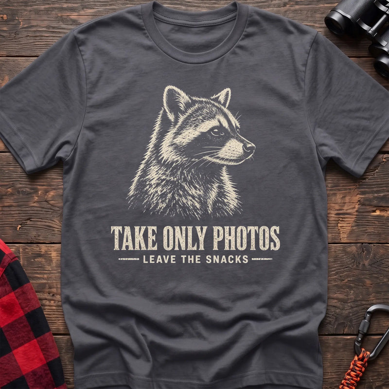 Charcoal cotton t-shirt with a raccoon graphic and Take Only Photos Leave the Snacks text on rustic wood
