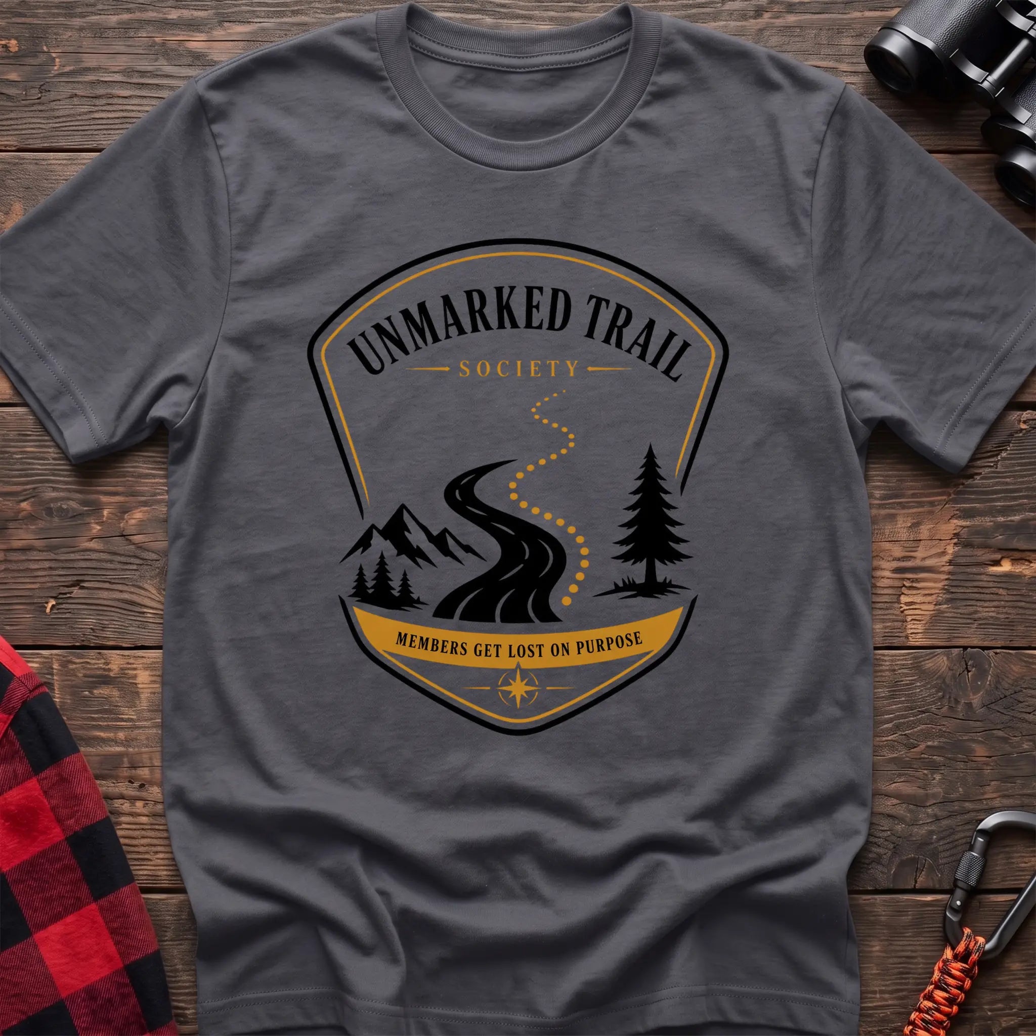 Charcoal cotton hiking t-shirt with Unmarked Trail Society badge, winding trail, mountains, pine trees, and "Members Get Lost on Purpose" text