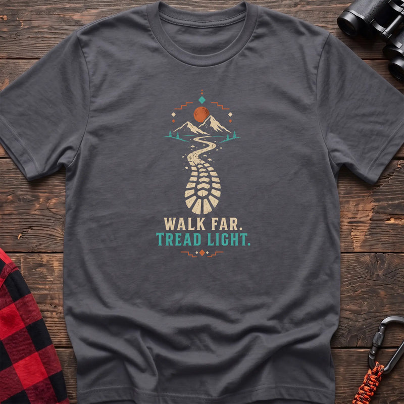 Charcoal cotton t-shirt with a bootprint trail and mountain graphic and Walk Far Tread Light text on rustic wood