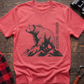 Coral silk t-shirt with a black illustration of a bear standing on mountain peaks, with the vertical text “ASCEND HIGHER” beside it, laid flat on a wooden surface.