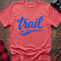 Coral silk cotton t-shirt with blue cursive trail script and dotted path graphic, flat lay on rustic wood with hiking gear