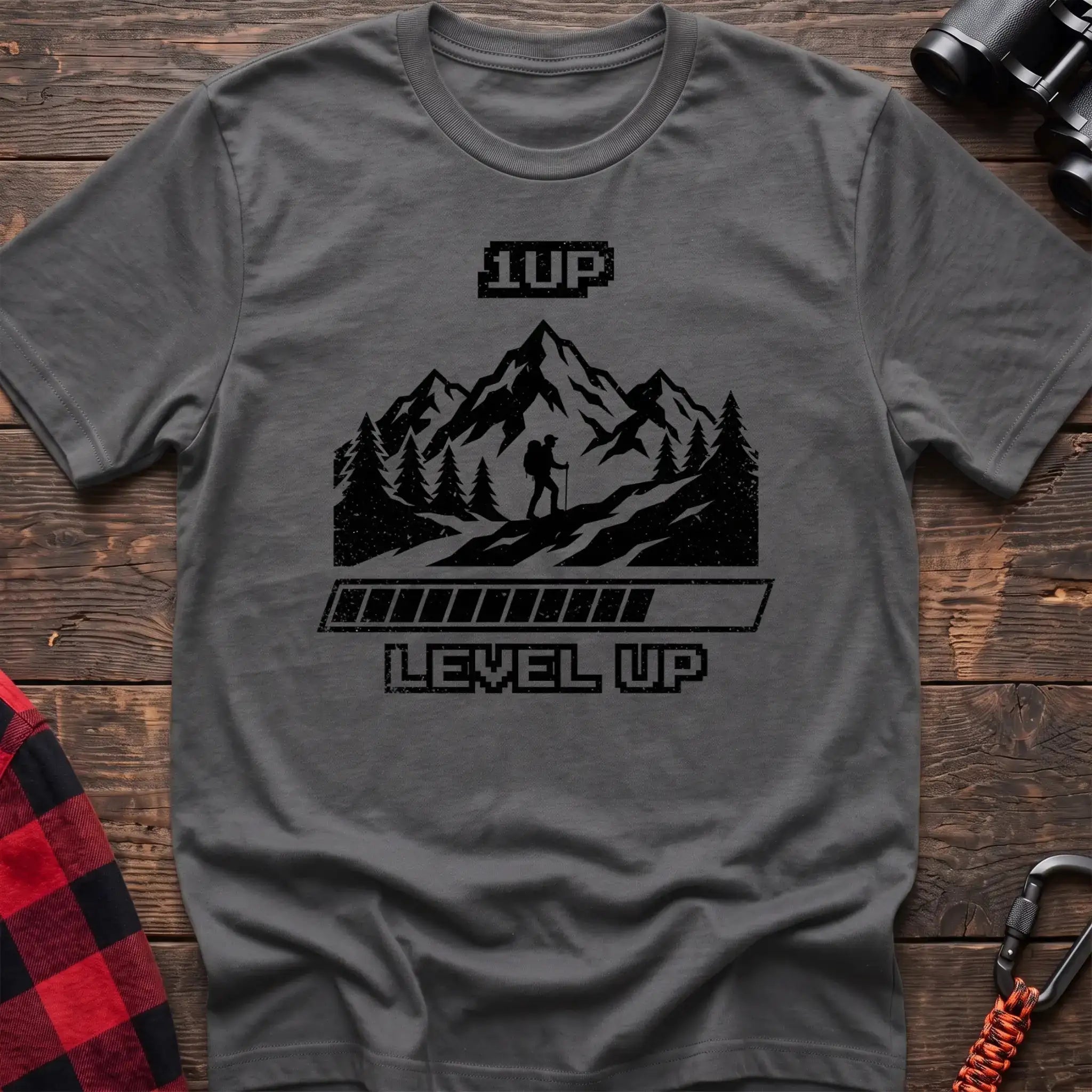 Graphite heather t-shirt with black graphic of a hiker on a mountain trail under pixel-style 1UP text and a progress bar reading Level Up