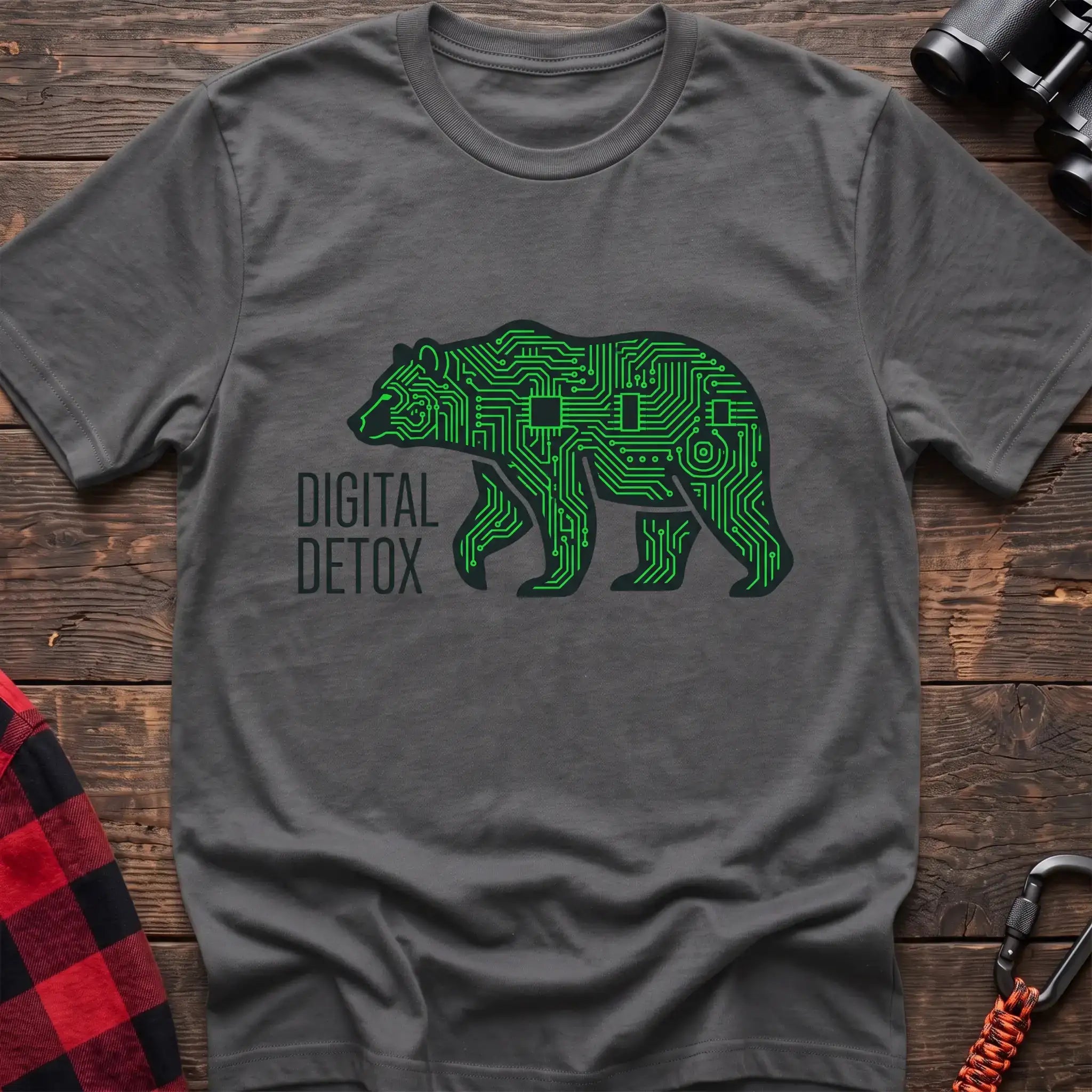 Graphite heather t-shirt with a neon green circuit-board patterned silhouette of a walking bear, and the text “DIGITAL DETOX” printed to the left of the design, laid flat on a wooden surface.