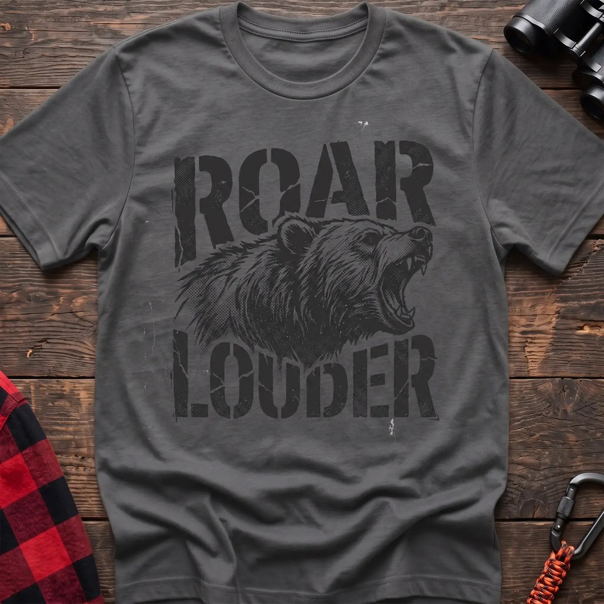 Graphite heather t-shirt with a distressed black graphic of a roaring bear head between the bold text “ROAR” and “LOUDER,” laid flat on a wooden surface.