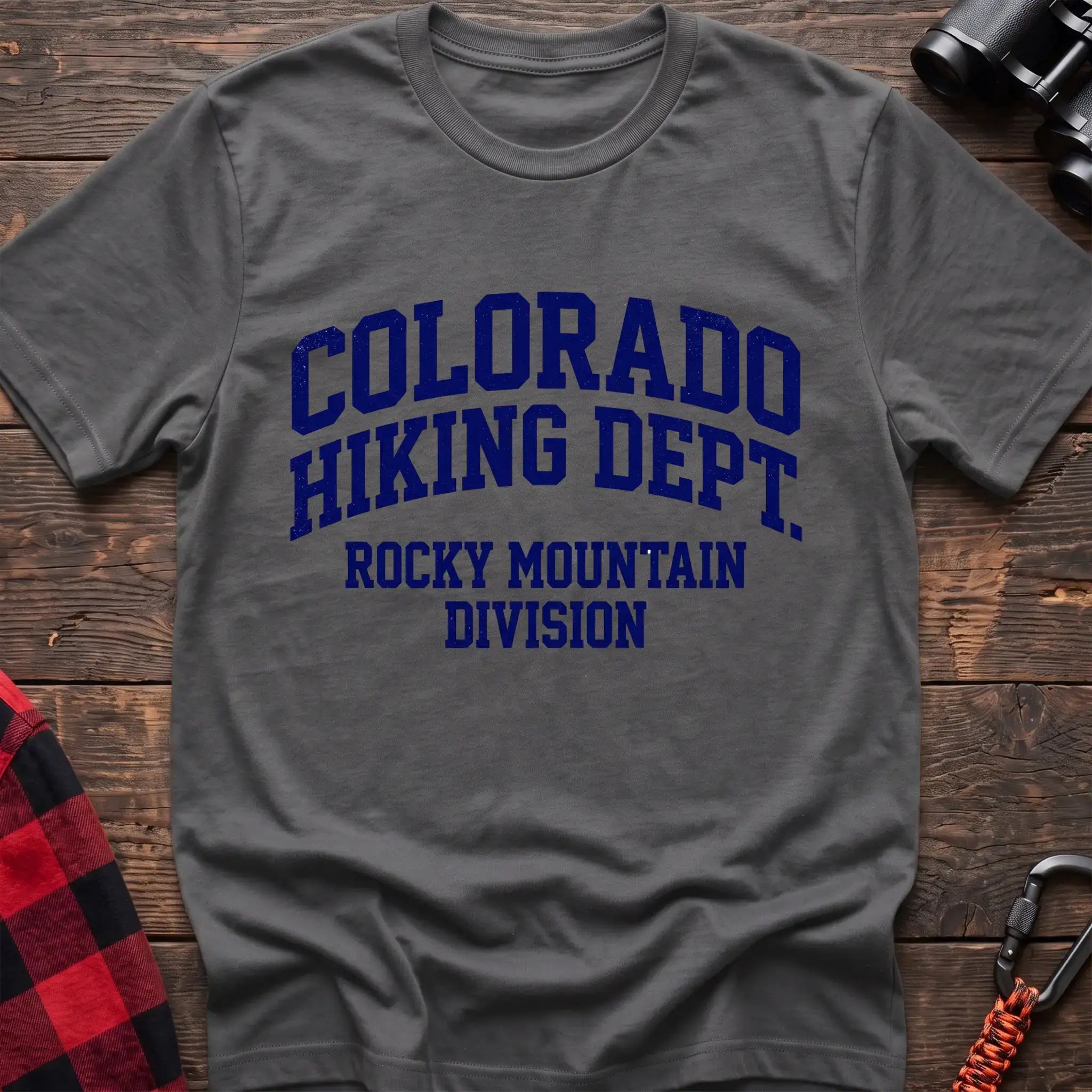 Graphite heather t-shirt with distressed dark blue collegiate-style text reading “COLORADO HIKING DEPT. ROCKY MOUNTAIN DIVISION,” laid flat on a wooden surface.