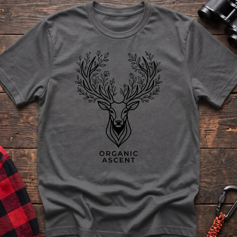 Graphite heather t-shirt with a black line drawing of a deer’s head whose antlers are formed from leafy branches and flowers, with the text “ORGANIC ASCENT” printed below, laid flat on a wooden surface.