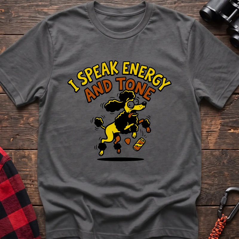 Graphite heather t-shirt with a cartoon yellow and black poodle jumping excitedly next to a falling energy drink can, with the arched text “I SPEAK ENERGY AND TONE,” laid flat on a wooden surface.