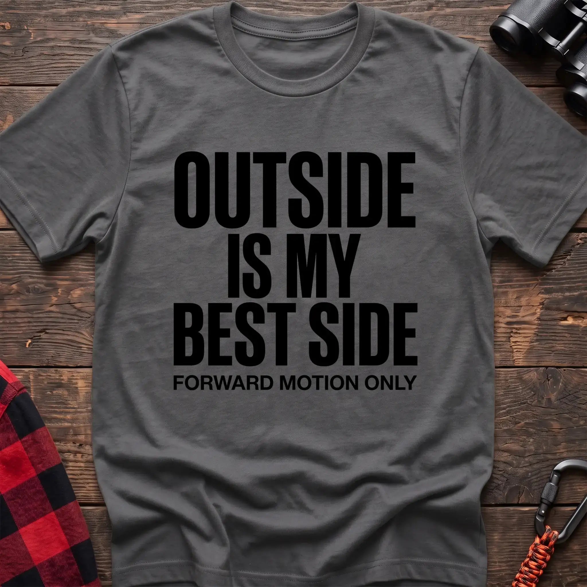 Graphite heather t-shirt with bold black text reading “OUTSIDE IS MY BEST SIDE” and “FORWARD MOTION ONLY” below it, laid flat on a wooden surface.