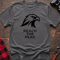 Graphite heather crew-neck t-shirt with a black stylized eagle head logo and the text “REACH THE PEAK” printed on the front