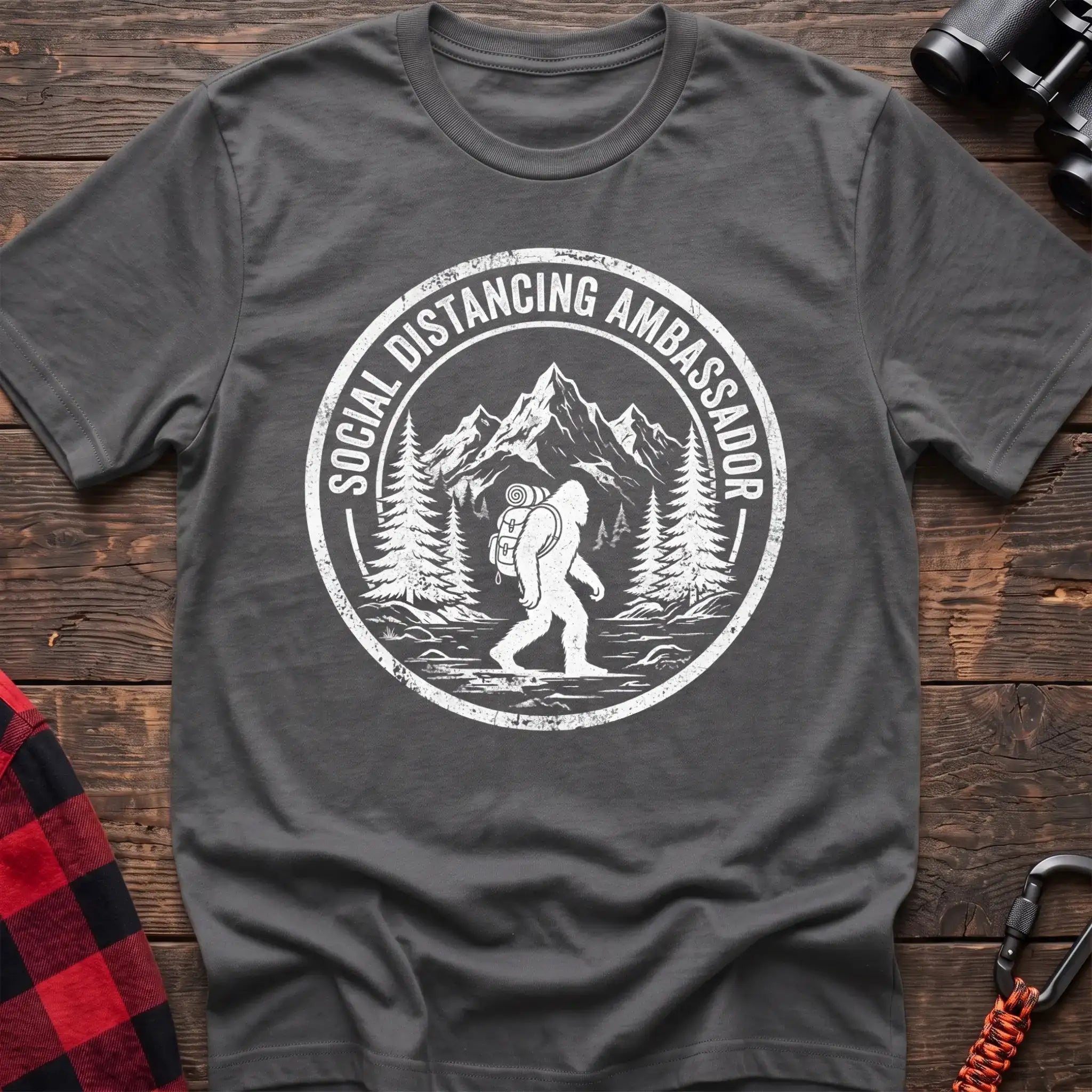 Graphite heather t-shirt with white circular badge graphic of Bigfoot hiking with a backpack through mountains and the text Social Distancing Ambassador