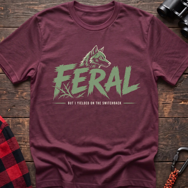 Heather maroon cotton t-shirt with a wolf graphic and Feral But I Yielded on the Switchback text on rustic wood