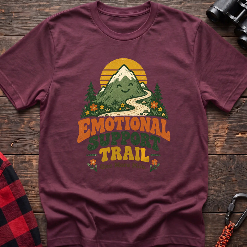 Heather maroon cotton t-shirt with a smiling mountain and trail graphic and Emotional Support Trail text on rustic wood