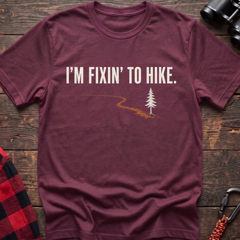 Heather maroon cotton t-shirt with a trail and pine graphic and I’m Fixin’ to Hike text on rustic wood