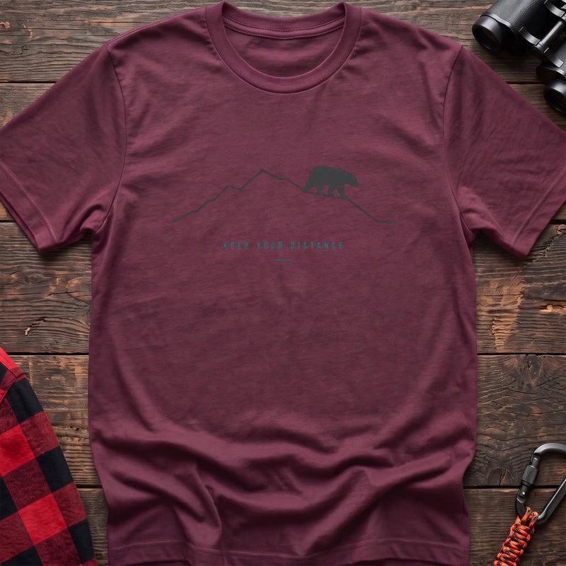 Heather maroon hiking t-shirt with a line-art mountain, walking bear, and the text “Keep Your Distance”